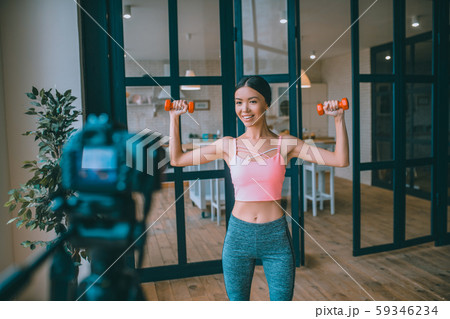 Slim dark-haired fitness trainer doing exercises with barbells Slim dark-haired fitness trainer doing exercises with barbells 59346234