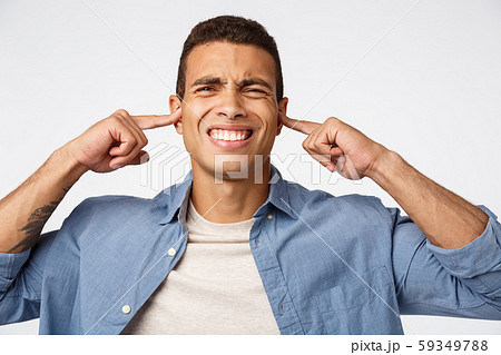 Disappointed upset man in blue shirt over t-shirt, grimacing from discomfort and dislike, cover ears 59349788