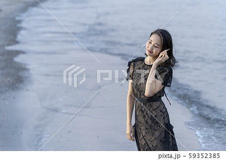 沖縄県石垣島の海辺波打ち際で貝殻を拾い波の音を聞く人魚のように美しい女性のライフスタイルの写真素材