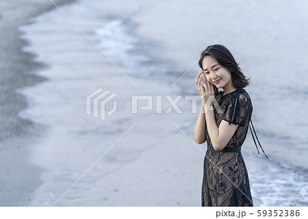 沖縄県石垣島の海辺波打ち際で貝殻を拾い波の音を聞く人魚のように美しい女性のライフスタイルの写真素材