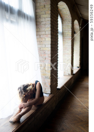 Beautiful ballerina in the black swimming suit posing on the large window in light hall. Concept of 59356249