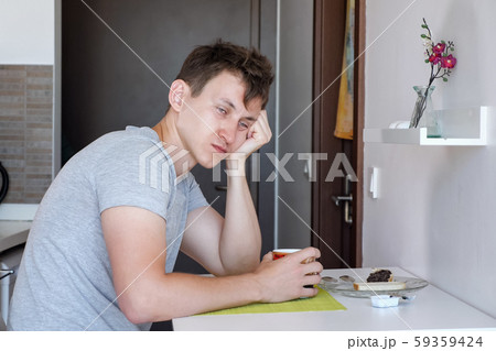 Sleepy man is having a cup of tea sitting at small kitchen in renting apartment on vacation. Sleepy man is having a cup of tea sitting at small kitchen in renting apartment on vacation. 59359424