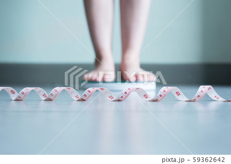 Blured of woman foot standing on weigh scales with measuring tape Blured of woman foot standing on weigh scales with measuring tape 59362642