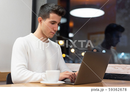 Young man working on his laptop in a coffee shop, young student typing on computer.  59362678