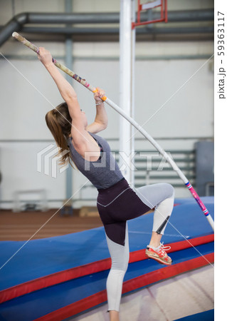 Pole vaulting indoors - young sportive woman with ponytail leaning on the pole and about to jump Pole vaulting indoors - young sportive woman with ponytail leaning on the pole and about to jump 59363117