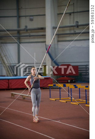 Pole vaulting indoors - young woman holding a pole looking up 59363152