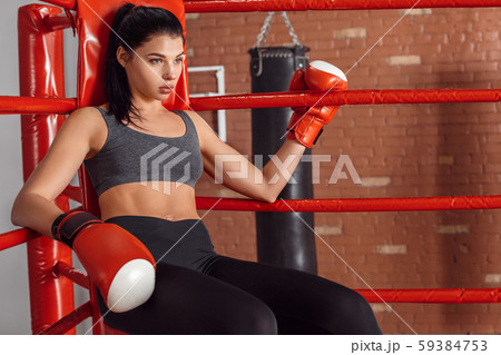 Boxing. Woman boxer in gloves sitting in the corner of ring leaning back tired 59384753