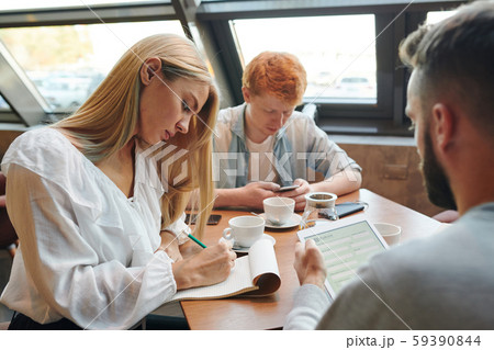 Two clever guys using gadgets while blonde girl making notes in notepad in cafe Two clever guys using gadgets while blonde girl making notes in notepad in cafe 59390844