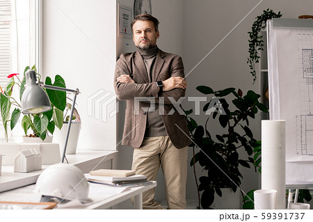 Serious architect or engineer in formalwear standing by workplace by window 59391737