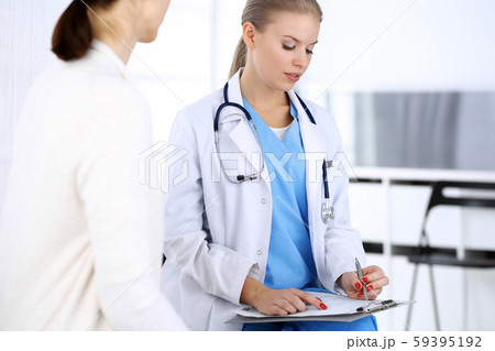 Doctor and patient during consultation. Physician at work filling up medication history record while Doctor and patient during consultation. Physician at work filling up medication history record while 59395192
