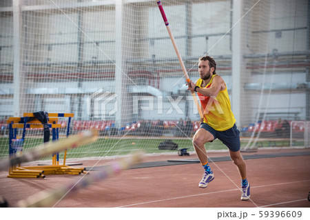Pole vaulting indoors - a athletic man in yellow shirt running on the track with a pole in the 59396609