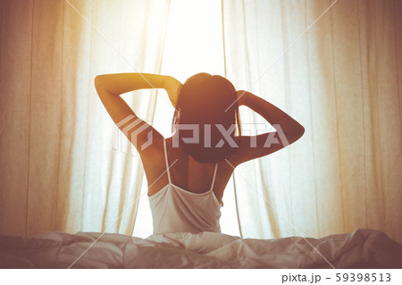Woman stretching hands in bed after wake up, sun flare . Brunette entering a day happy and relaxed Woman stretching hands in bed after wake up, sun flare . Brunette entering a day happy and relaxed 59398513
