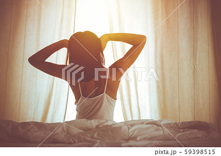 Woman stretching hands in bed after wake up, sun flare . Brunette entering a day happy and relaxed 59398515