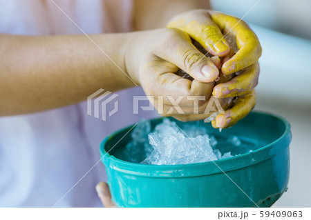 Close up to wash hands stained with yellow oil color by ice in a green bowl. 59409063