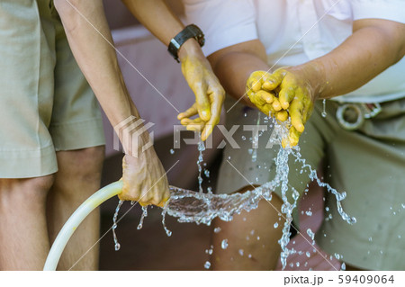 Student holding garden hose spraying water from white rubber tube to wash hands stained with yellow oil color. Student holding garden hose spraying water from white rubber tube to wash hands stained with yellow oil color. 59409064