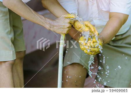 Student holding garden hose spraying water from white rubber tube to wash hands stained with yellow oil color. Student holding garden hose spraying water from white rubber tube to wash hands stained with yellow oil color. 59409065