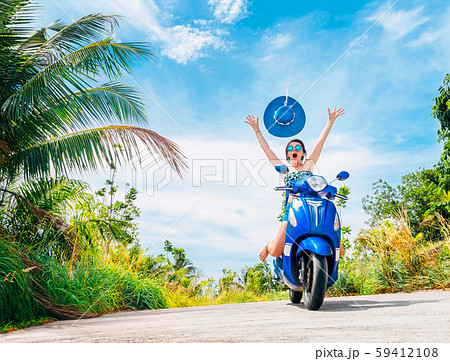 Crazy funny woman with flying hair riding a motorbike on a blue sky and green tropics background 59412108