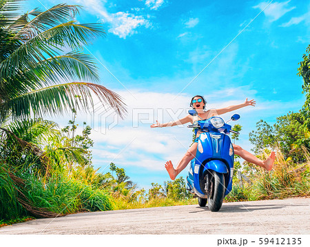 Crazy funny woman with flying hair riding a motorbike on a blue sky and green tropics background 59412135