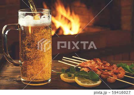 Pouring beer into a mug, shrimp fried on skewers with arugula, lemon on a black slate dish on a 59416027