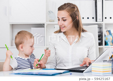 Female employee is working on laptop while child painting on papers 59425167