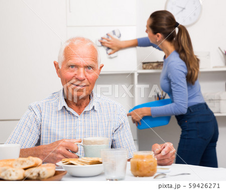 Elderly man drinkimg tea, daughter washing furniture kitchen at home Elderly man drinkimg tea, daughter washing furniture kitchen at home 59426271
