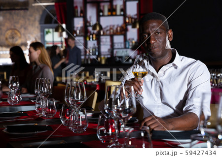 African-american man with glass of white wine in a luxury restaurant African-american man with glass of white wine in a luxury restaurant 59427434