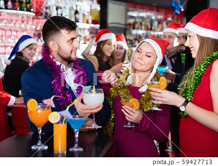 Man and two women with cocktails in Santa hats celebrating at nightclub 59427713