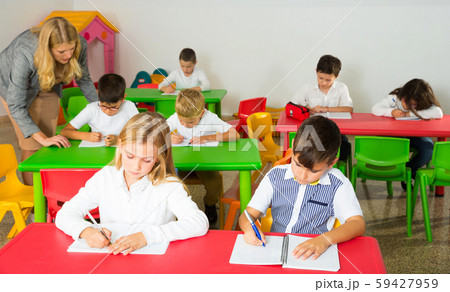 Schoolkids working and teacher helping them Schoolkids working and teacher helping them 59427959