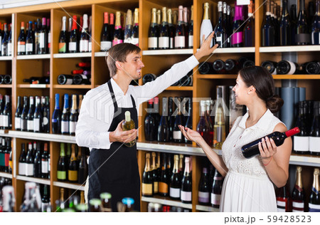 portrait of male seller showing bottle of wine to female customer in wine shop portrait of male seller showing bottle of wine to female customer in wine shop 59428523