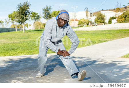 Athletic african american male performs warm-up exercises in park 59429497