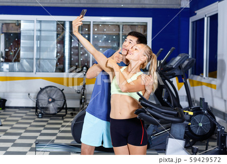Smiling athletic pair making selfie during break in workout session at gym Smiling athletic pair making selfie during break in workout session at gym 59429572