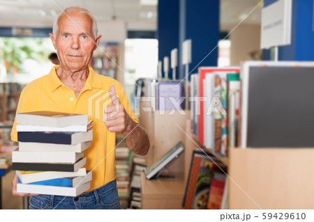 Senior male with pile of books holding thumb up in library Senior male with pile of books holding thumb up in library 59429610