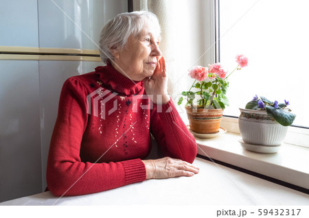 Old lonely woman sitting near the window in his house. 59432317