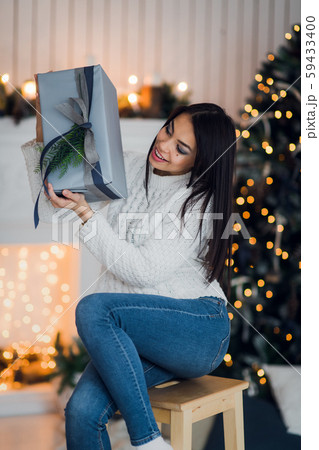 Happy woman Excited To Open Christmas Present sitting at home in front of a christmas tree and Happy woman Excited To Open Christmas Present sitting at home in front of a christmas tree and 59433400