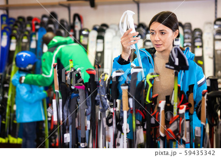 Attractive girl choosing ski poles for skiing in store of sports equipment Attractive girl choosing ski poles for skiing in store of sports equipment 59435342