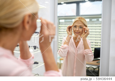 Long-haired woman looking in the mirror to choose glasses frame Long-haired woman looking in the mirror to choose glasses frame 59436444