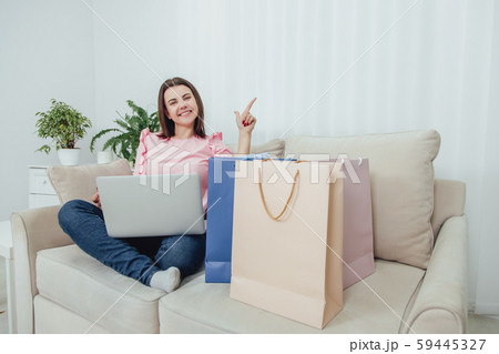 Pretty girl sitting on the sofa, at home, using laptop for shopping online, pointing finger up Pretty girl sitting on the sofa, at home, using laptop for shopping online, pointing finger up 59445327