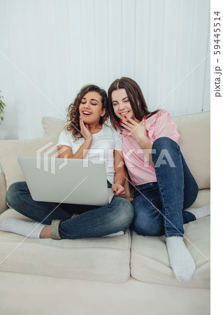 Excited girls sitting on the sofa with crossed legs watching film on the laptop. Excited girls sitting on the sofa with crossed legs watching film on the laptop. 59445514