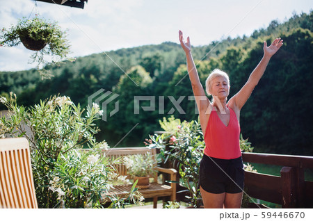 A senior woman standing outdoors on a terrace in summer, doing exercise. A senior woman standing outdoors on a terrace in summer, doing exercise. 59446670