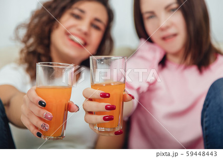 Blurred afro-american and caucasian girl friends holding glasses of fresh juice in front of the 59448443