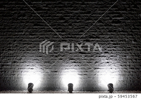 スポットライトで照らされ浮かび上がる黒いゴツゴツしたテクスチャのブロック壁の写真素材