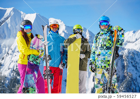 Image of two sports women and two men with skis and snowboard standing at ski resort 59456527