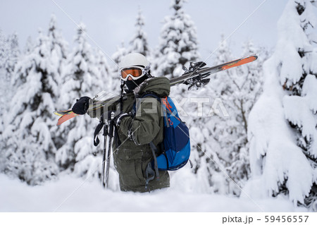 Photo of athlete in helmet and mask with skis on his shoulder against background of trees in snow Photo of athlete in helmet and mask with skis on his shoulder against background of trees in snow 59456557