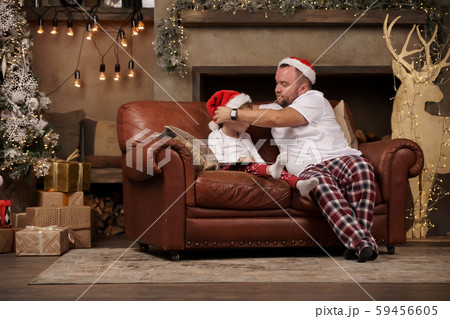 Image of father in Santa hat and son on red sofa in room Image of father in Santa hat and son on red sofa in room 59456605