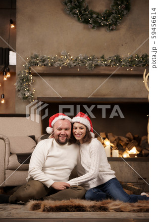 Photo of man and woman in Santa's caps sitting on floor in room Photo of man and woman in Santa's caps sitting on floor in room 59456614
