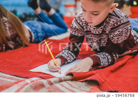 Happy child in knitted reindeer sweater, sealing envelope to Santa with Christmas presents wish list Happy child in knitted reindeer sweater, sealing envelope to Santa with Christmas presents wish list 59456768