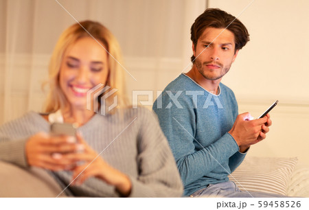 Suspicious Man Watching Girlfriend Texting On Phone Sitting At Home 59458526