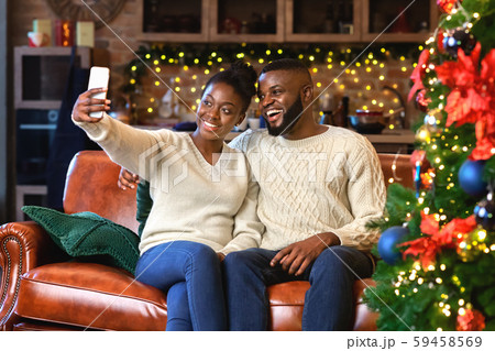 Happy black couple taking selfie sitting in decorated living room 59458569