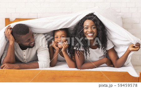 Mother, father and daughter hiding under blanket, having fun together 59459578