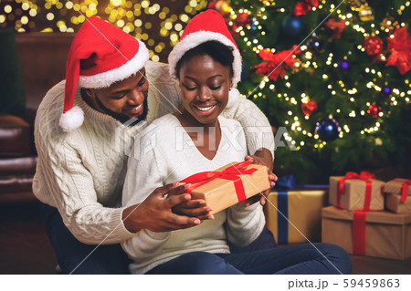 Happy afro girl receiving Christmas gift from her caring boyfriend Happy afro girl receiving Christmas gift from her caring boyfriend 59459863